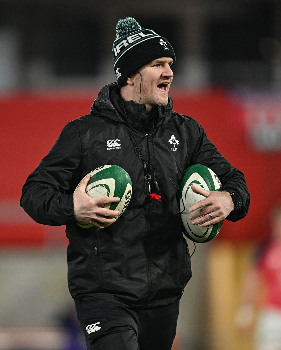 Rugby player running on field holding two rugby balls, shouting.