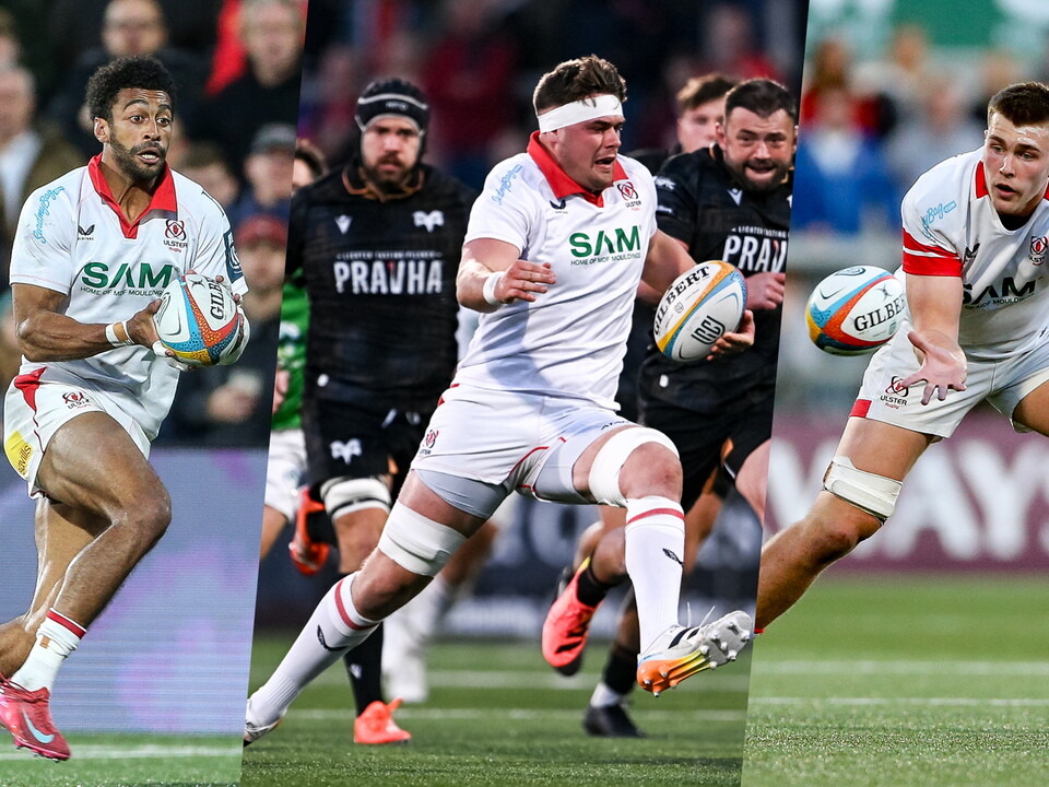 Three rugby players on a field, one running, one chasing, one kicking, with spectators in the background.