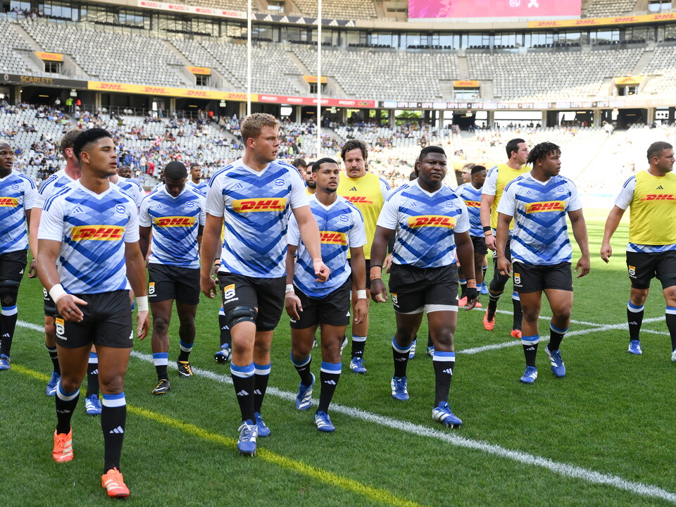 Rugby players wearing blue and white striped shirts walk onto the field.